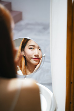 亚洲女人在家里对着镜子化妆。反思视角。
