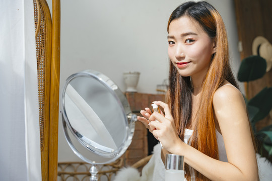 看着镜子，美丽的年轻亚洲女人用化妆品化妆。