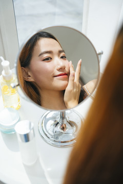 年轻的亚洲女人在镜子前化妆。