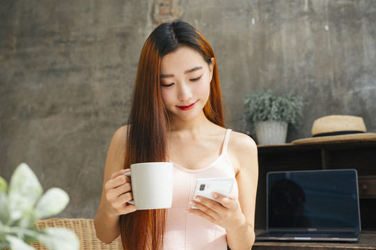 年轻的亚洲女性早餐喝咖啡，在社交媒体上读东西。