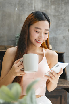 快乐的年轻亚洲女性在社交媒体上看一些有趣的事情，喝咖啡。
