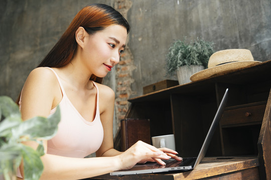 年轻的亚洲女性在家工作时使用笔记本电脑。