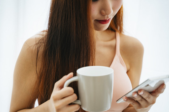 美丽的亚洲女人，带着一杯咖啡和智能手机。