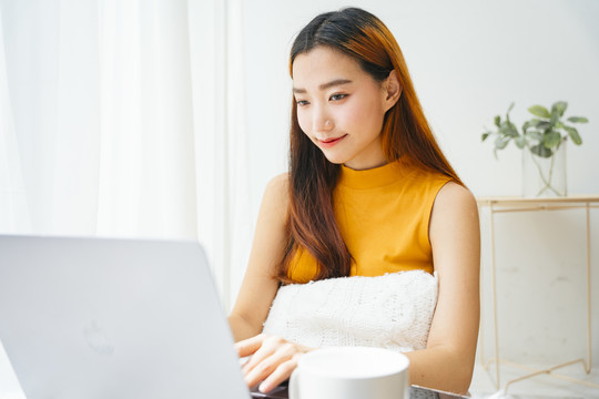 一位年轻的亚洲妇女在白屋子里用笔记本电脑工作。