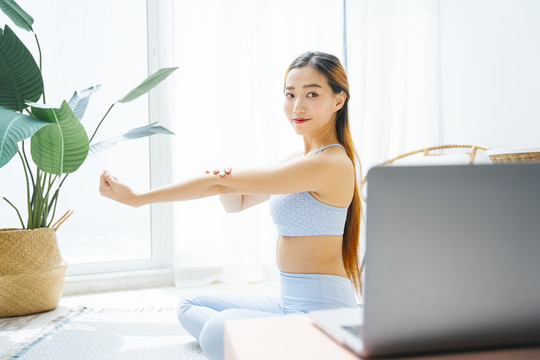 美丽的运动型女士在网上讲授瑜伽课程。她在笔记本电脑上看在线瑜伽课。