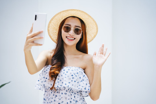 美丽的亚洲女旅行者戴着太阳镜，戴着帽子，用智能手机聊天。