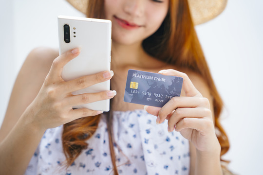 年轻漂亮的女旅行者用信用卡和智能手机付账单。