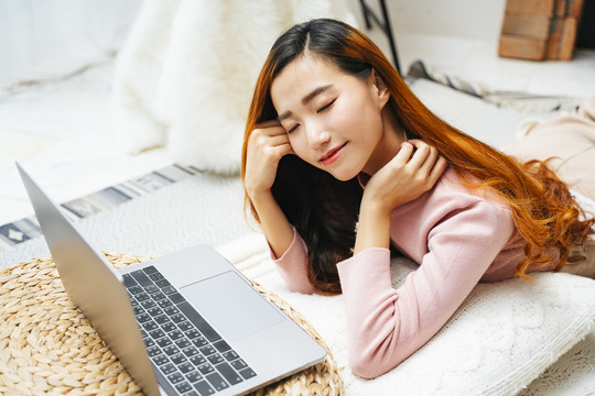 美丽的亚洲年轻女子一边看笔记本电脑一边睡觉。