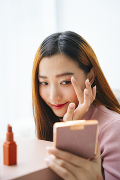 美丽的亚洲女人在化妆，看着便携式镜子。
