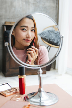 美丽的亚洲女人在镜子前涂口红。