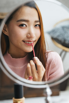 美丽的亚洲女人在镜子前涂口红。