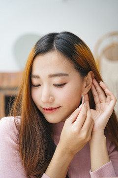 美丽的亚洲女人在家戴着耳环。