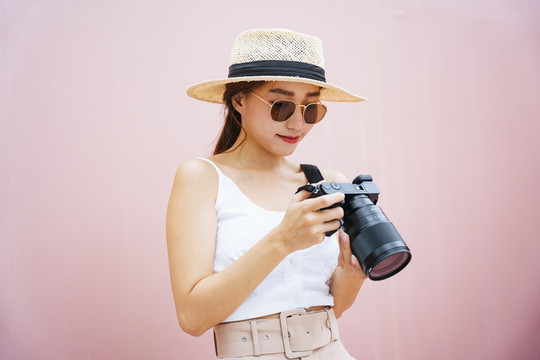 美丽的亚洲摄影师戴着太阳镜，戴着帽子，手持数码相机。