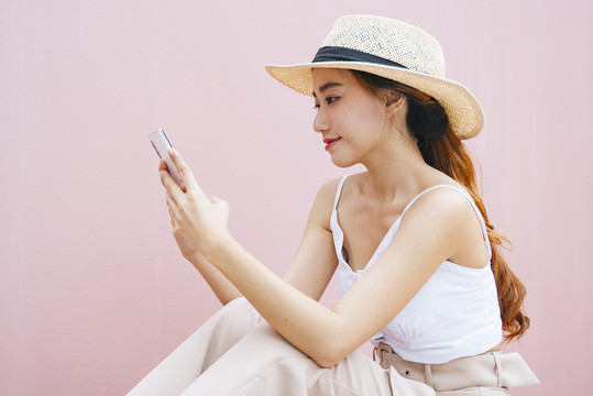 侧视图-美丽的亚洲女性戴着粉色背景的智能手机隔离帽。