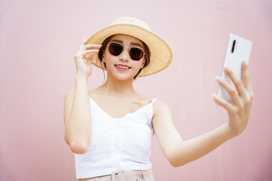 戴着帽子、戴着太阳镜、手持智能手机的美丽亚洲年轻女子的肖像。