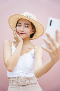 戴帽子的亚洲美女用智能手机自拍。