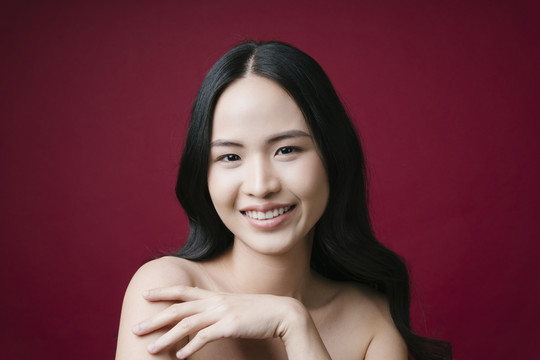 美丽的亚洲女性健康的皮肤概念自然化妆隔离红色背景。