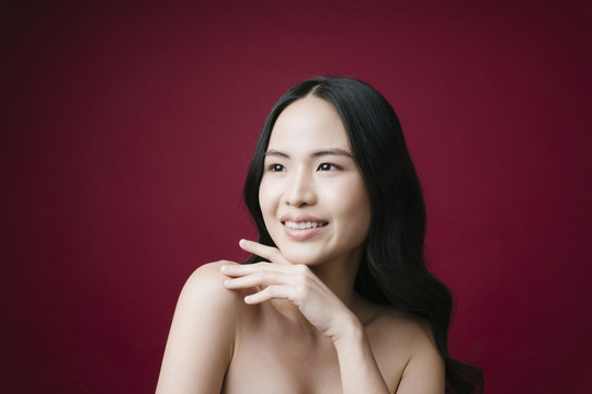 美丽的亚洲女性健康的皮肤概念自然化妆隔离红色背景。