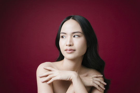 美丽亚洲女性的肖像黑头发自然健康的皮肤隔离在红色背景上。