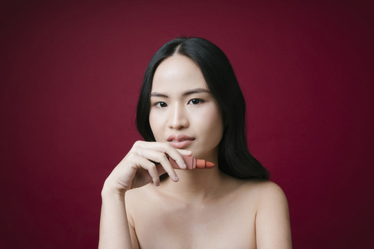 美丽的亚洲年轻女子的肖像，红色的头发上夹着粉红唇膏，红色背景。