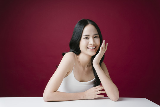 美丽的年轻亚洲女性，自然化着妆，在红色背景上看着镜头。