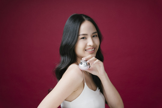 一位年轻美丽的女士手持一罐隔离在红色背景上的奶油化妆品的肖像。