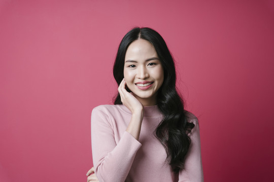 粉红色背景上微笑的年轻亚洲女性肖像。
