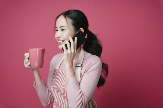 一幅年轻的亚洲女性在打电话，拿着一杯粉红色背景的咖啡的照片。