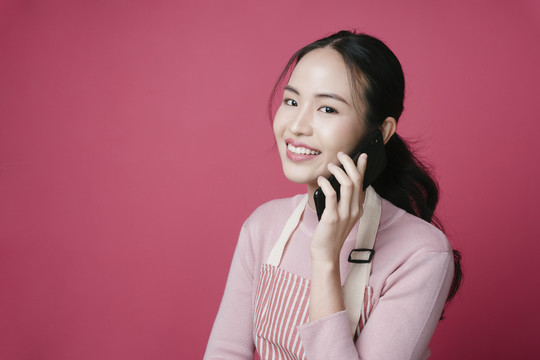 粉红色背景下，年轻的亚洲女性在电话中交谈的肖像。
