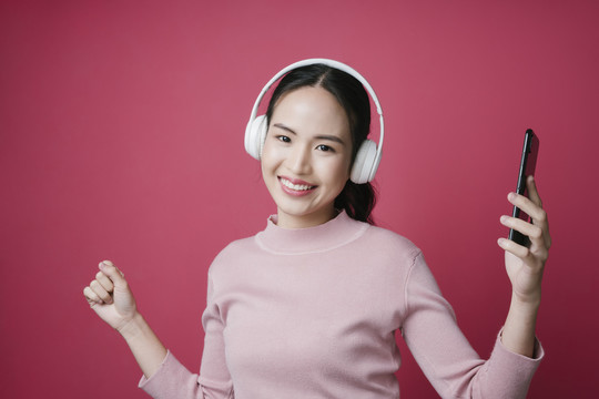 一位年轻的亚洲女性的肖像，她喜欢在粉色背景上听音乐。