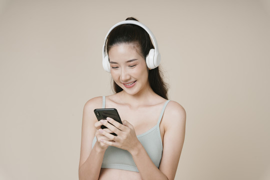 亚洲运动女性运动员肖像，使用智能手机，通过无线耳机收听音乐。