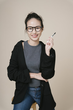 亚洲女商人的肖像穿着黑色夹克，戴着米色背景的眼镜。