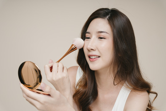 美丽的年轻亚洲女性在脸上涂抹化妆粉的肖像。