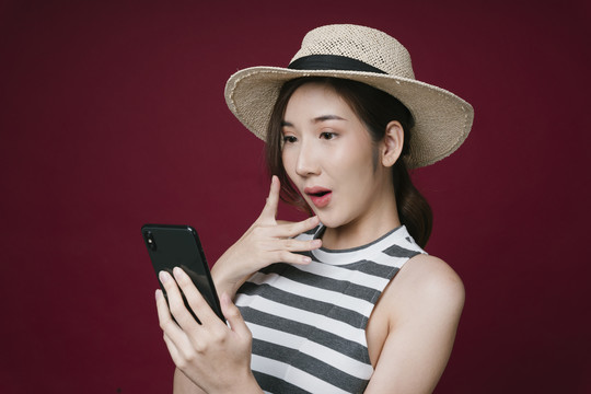 快乐的亚洲年轻女子戴着智能手机的帽子。网上购物和预订的概念。