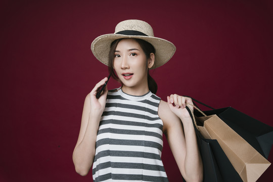 亚洲年轻女子的肖像，手持纸袋，手持智能手机，享受网上购物。