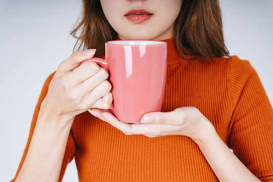 一位身穿橙色毛衣的亚洲妇女，手拿咖啡杯或杯子的模型。