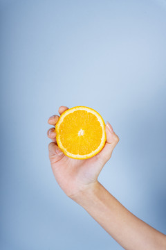 一个女人的手拿着蓝色背景上的一片橘子。