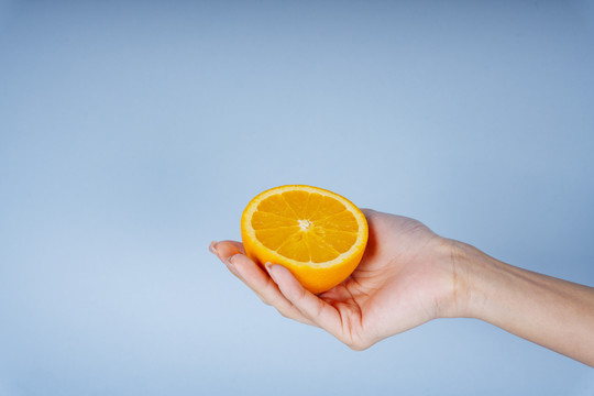 一个女人的手拿着蓝色背景上的一片橘子。