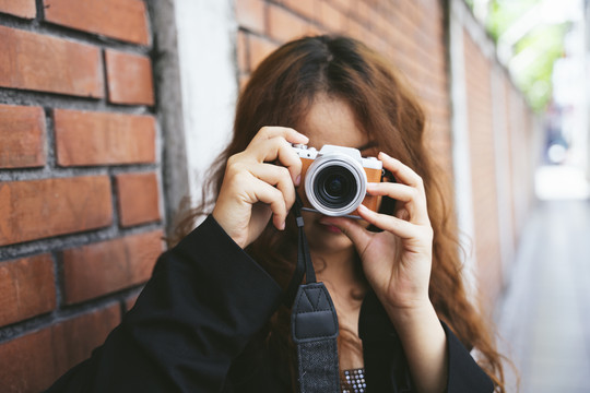 穿着黑色夹克的年轻亚洲女性用相机拍照的时尚肖像。