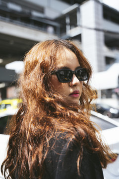 特写镜头-年轻的亚洲女人戴着太阳镜和黑色夹克在街上的时尚肖像。