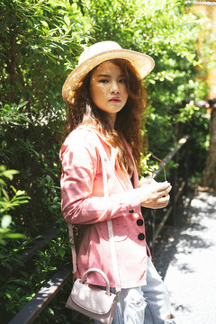 公园里穿着粉色夹克和帽子的年轻亚洲女性的时尚肖像。