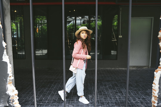 穿着粉色夹克和帽子在街上行走的年轻亚洲女性的时尚肖像。