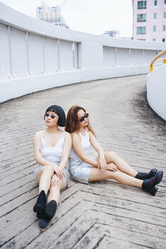 两名穿着白色背心和太阳镜坐在路上的年轻亚洲女性的肖像。
