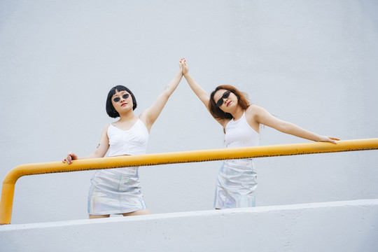 在阳台上，两位年轻的亚洲女性穿着白色背心，戴着墨镜。