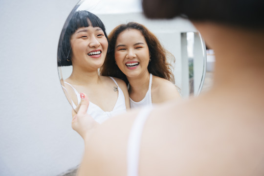 两位快乐的年轻亚洲女性对着镜子微笑的肖像。
