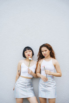 两位年轻的亚洲女性穿着白色背心手持鲜花的肖像。