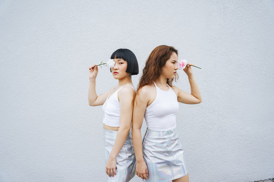 两位年轻的亚洲女性穿着白色背心手持鲜花的肖像。