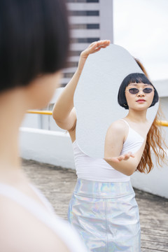年轻的亚洲短发女人戴太阳镜照镜子的肖像。
