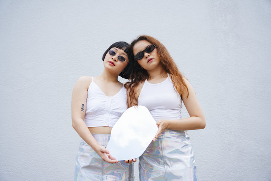 两位亚洲年轻女性的肖像，身穿白色背心，戴着墨镜，手持镜子。