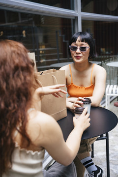 照片中的年轻亚洲女性戴着墨镜在咖啡馆和朋友聊天。